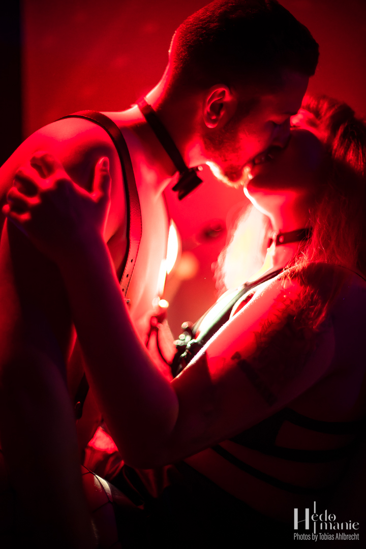 Close red-lit portrait of two performers.